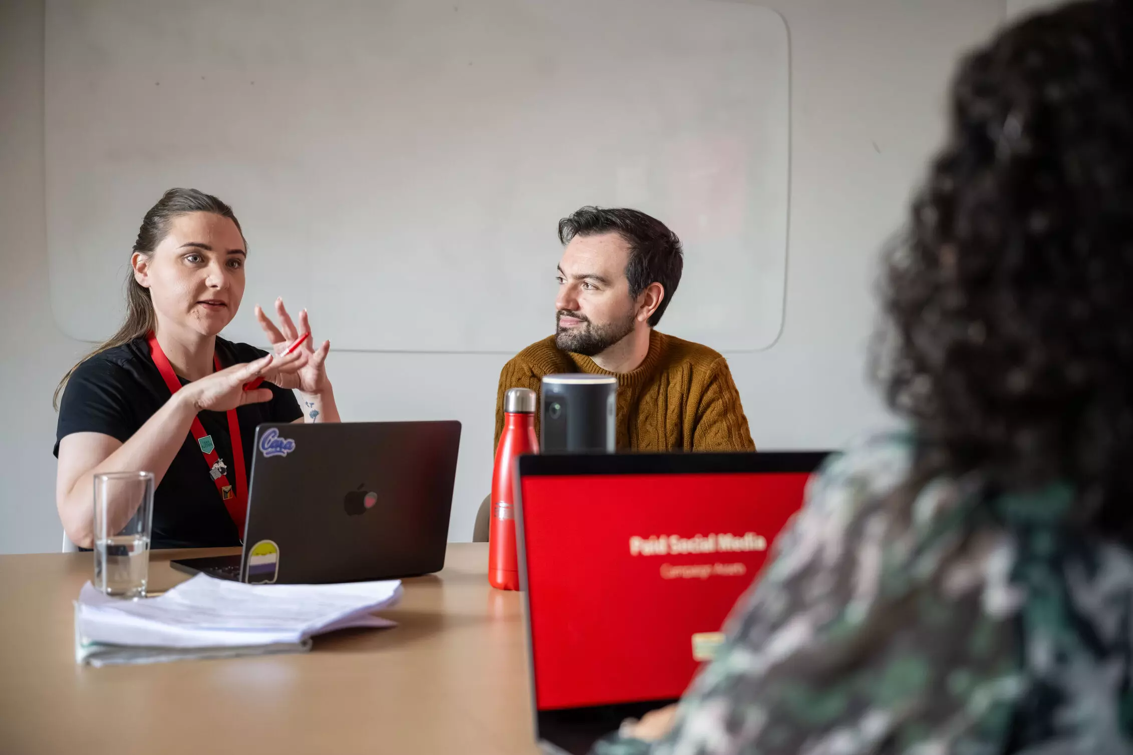 Customer Experience A man and woman wearing headphones are sitting at a desk with a laptop, surrounded by office furniture in an indoor setting.
